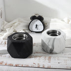 Two geometric fire pits, one black and one with a marble pattern, on a wooden surface with an alarm clock in the background.