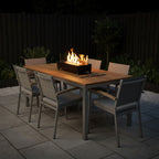 Outdoor dining table with chairs and Apollo Tabletop Fireplace in a garden setting at night.