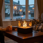Person holding a mug by a table with a glass fire pit, cosy indoor setting