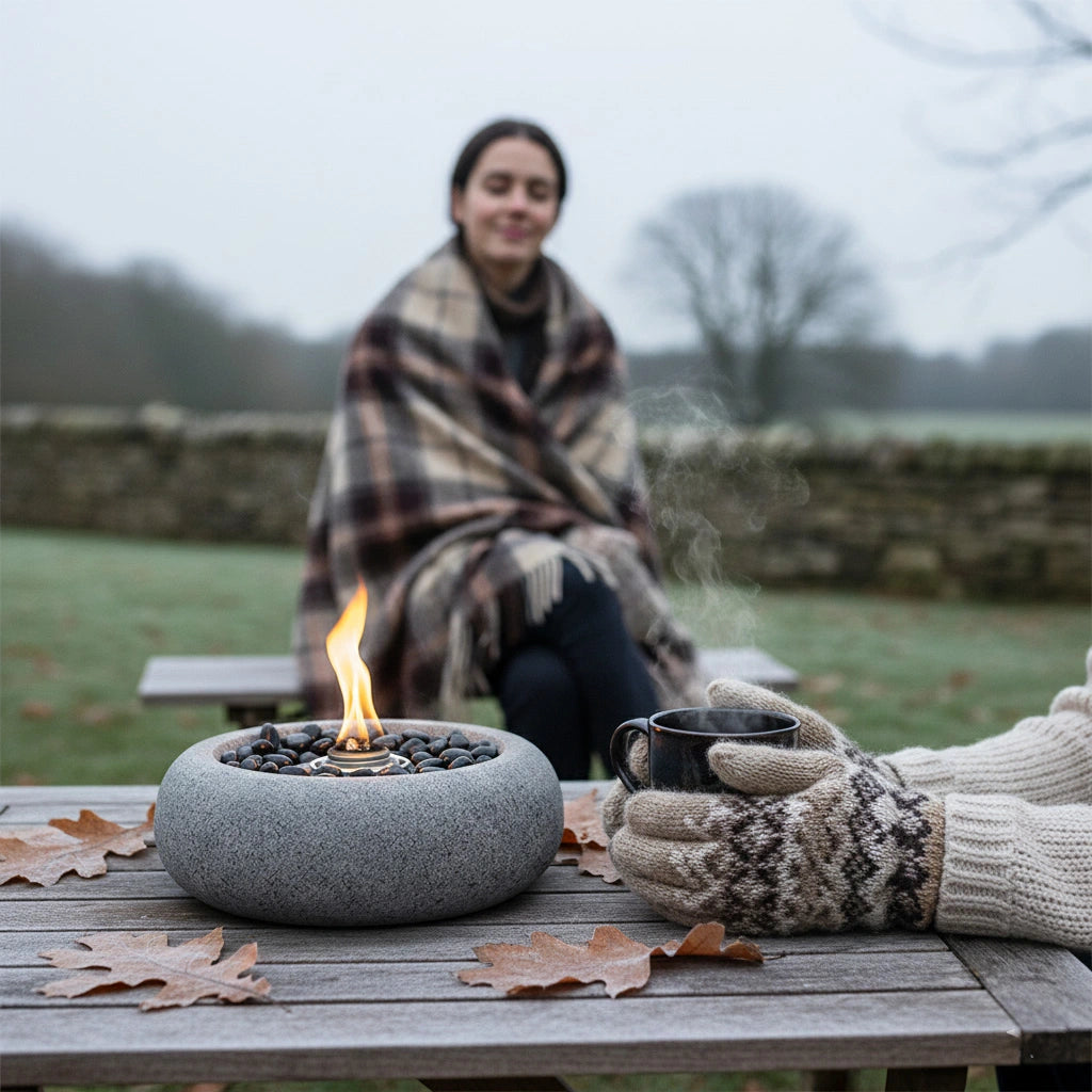 Person sitting outdoors with our gaia fire pit and hot drink, wearing a blanket and gloves.